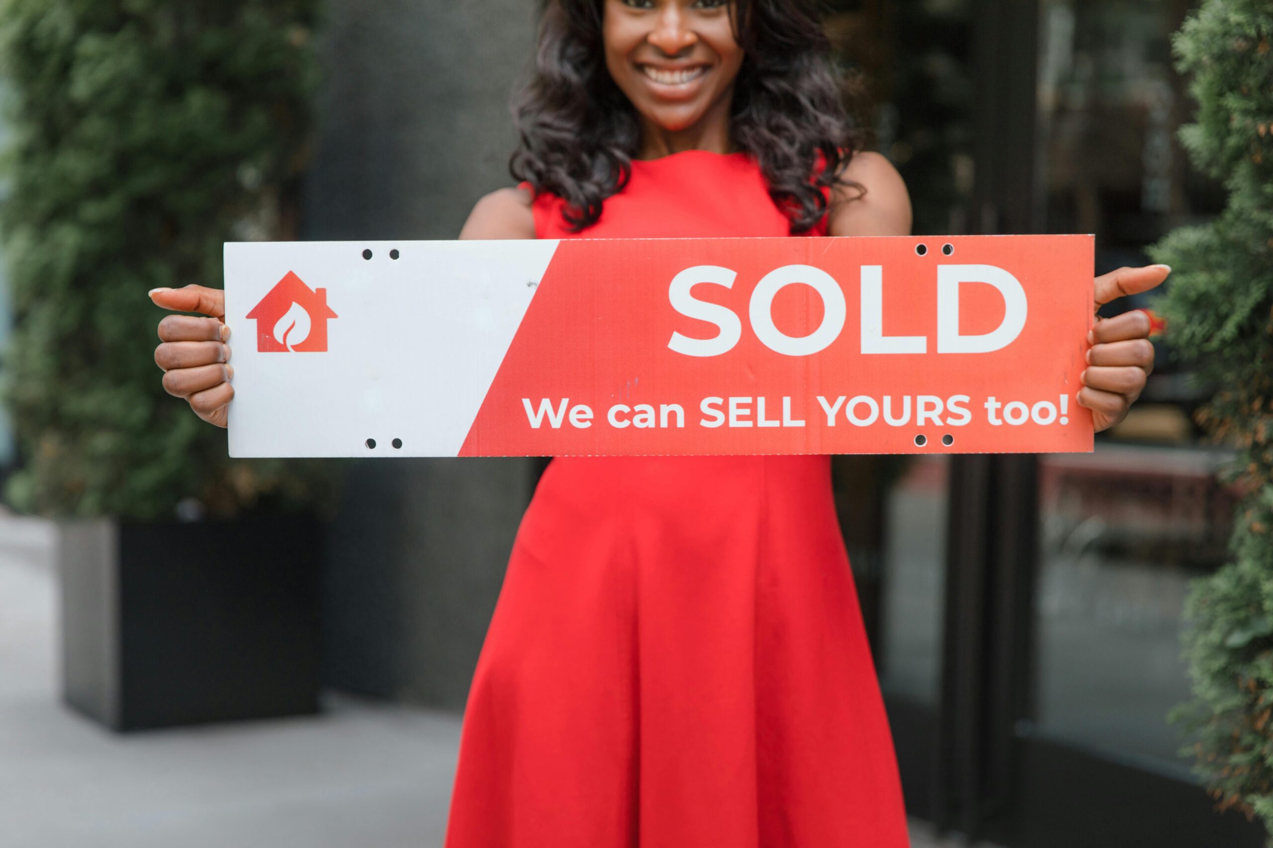 Smiling woman holding a 'Sold' sign, symbolizing successful real estate sales.