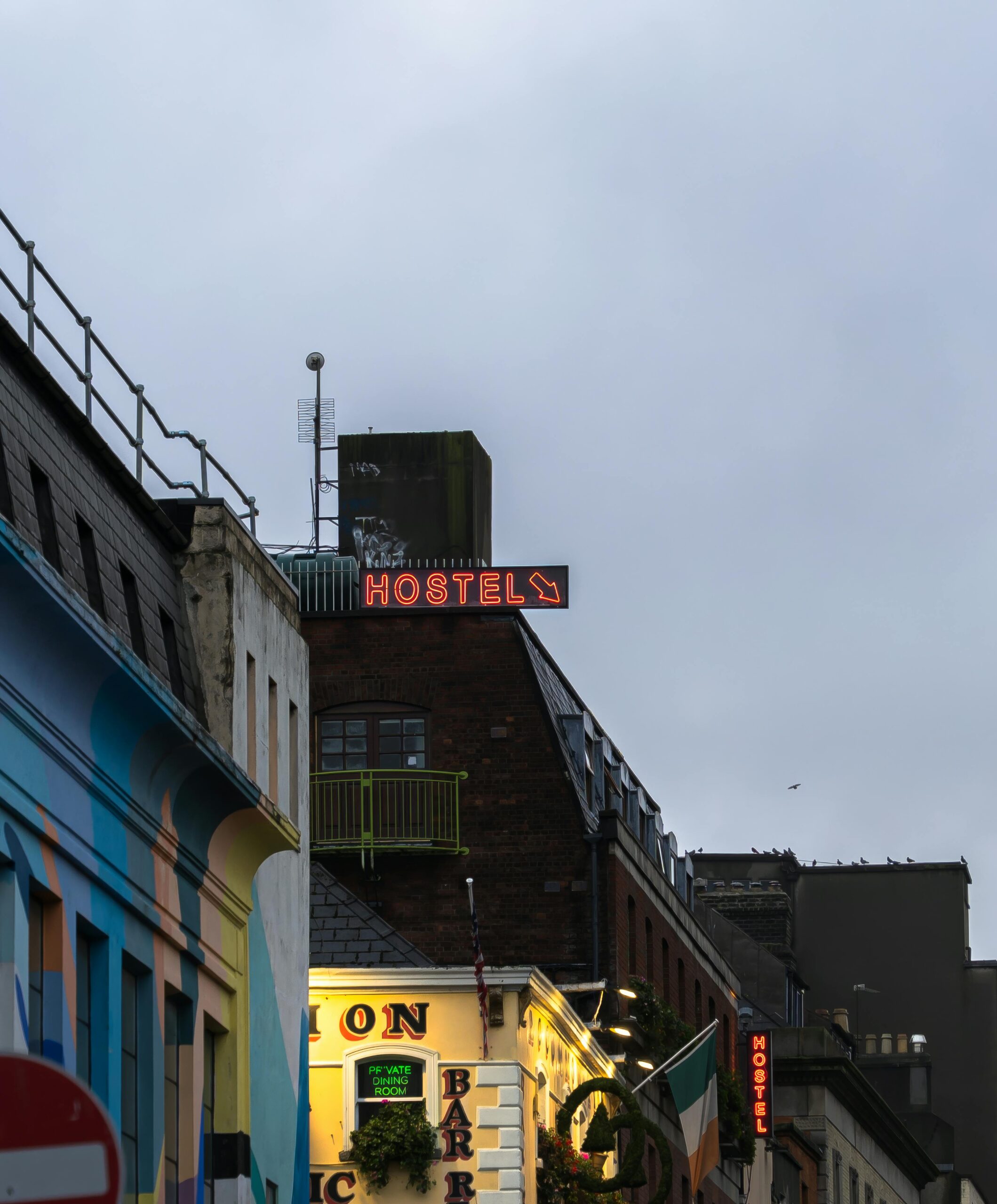 Colorful urban scene featuring a vibrant 'Hostel' sign on a city street during dusk.