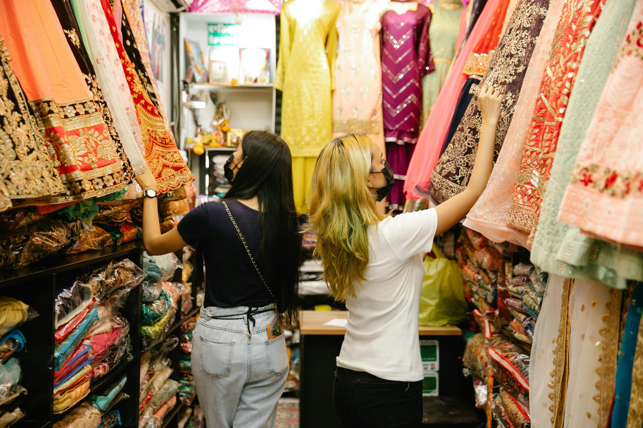 Two women browsing colorful traditional dresses in a boutique store.